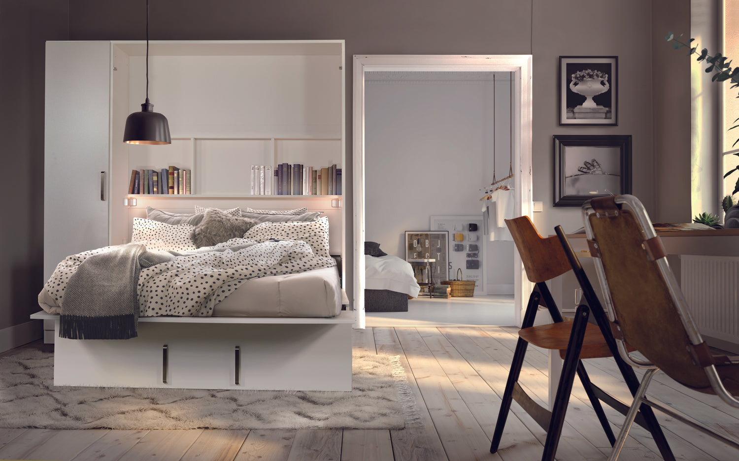 Lit escamotable blanc ouvert avec étagères intégrées, entouré de décor moderne et chaises en bois, dans une chambre lumineuse