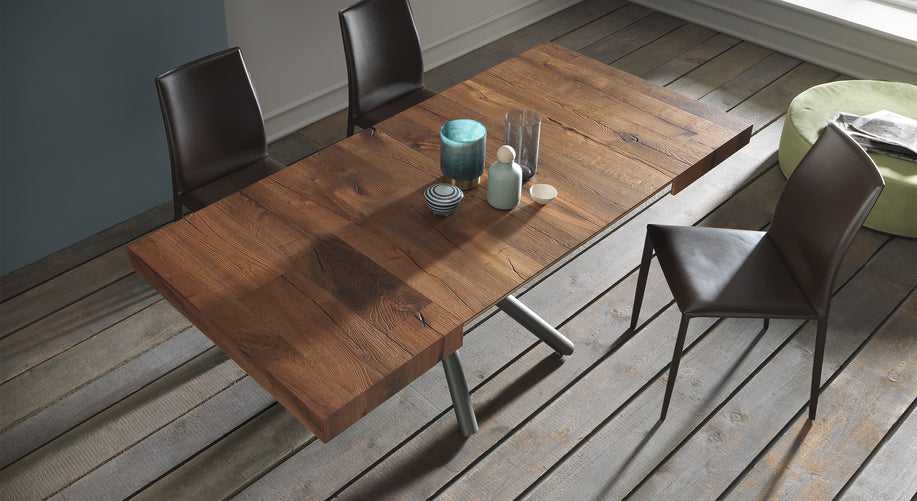 Table extensible Levante en bois, ouverte, entourée de chaises modernes, avec des objets décoratifs sur un sol en bois