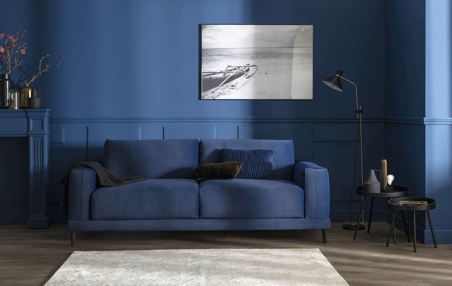 Canapé en velours bleu océan dans un salon élégant, avec des murs assortis, une photo en noir et blanc et des tables d'appoint modernes