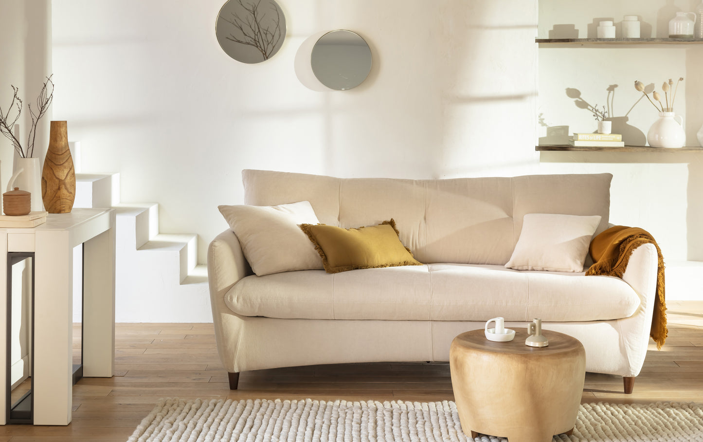 Canapé convertible beige avec coussins, table basse en bois, décor minimaliste et lumineux, ambiance chaleureuse et moderne