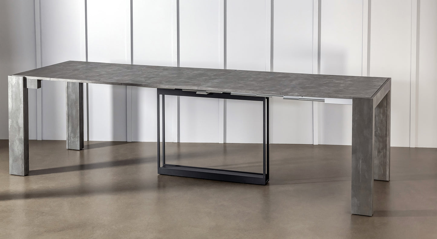 Table extensible compacte en métal gris, ouverte, dans un intérieur moderne avec sol en béton et mur blanc
