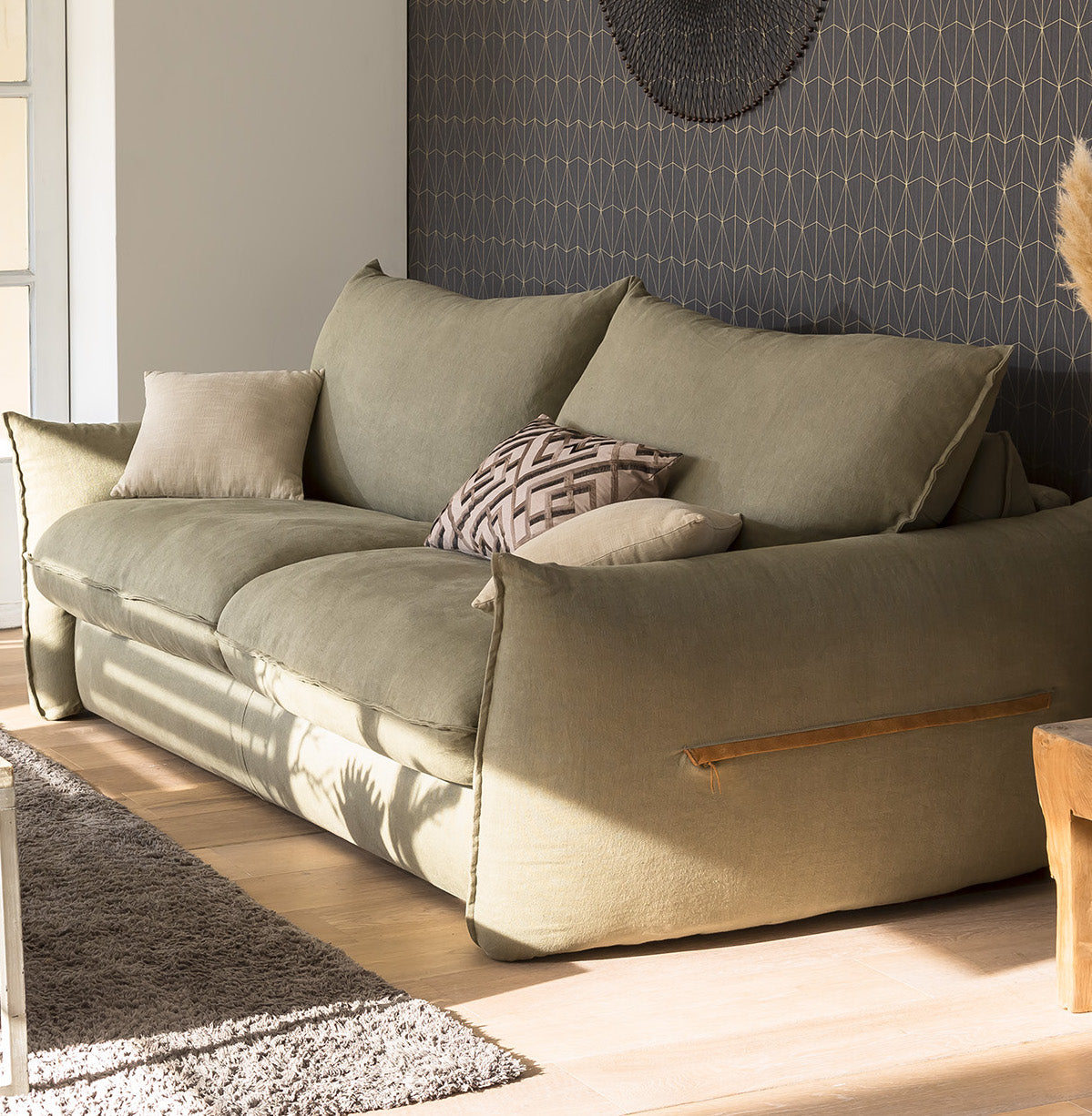 Canapé en lin vert avec coussins, éclairé par la lumière naturelle, dans un salon moderne au décor géométrique
