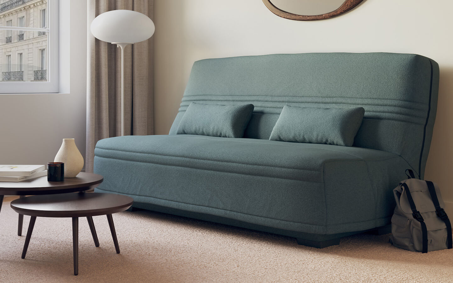 Canapé clic-clac en tissu bleu lagon dans un salon moderne, avec table basse, lampe et sac à dos. Fenêtre avec vue urbaine