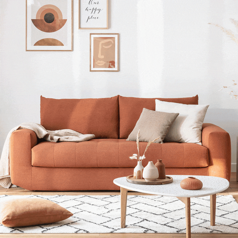 Canapé orange avec coussins beiges et blancs, table basse avec vases, décor mural abstrait et texte "Our happy place". Contexte "stella"