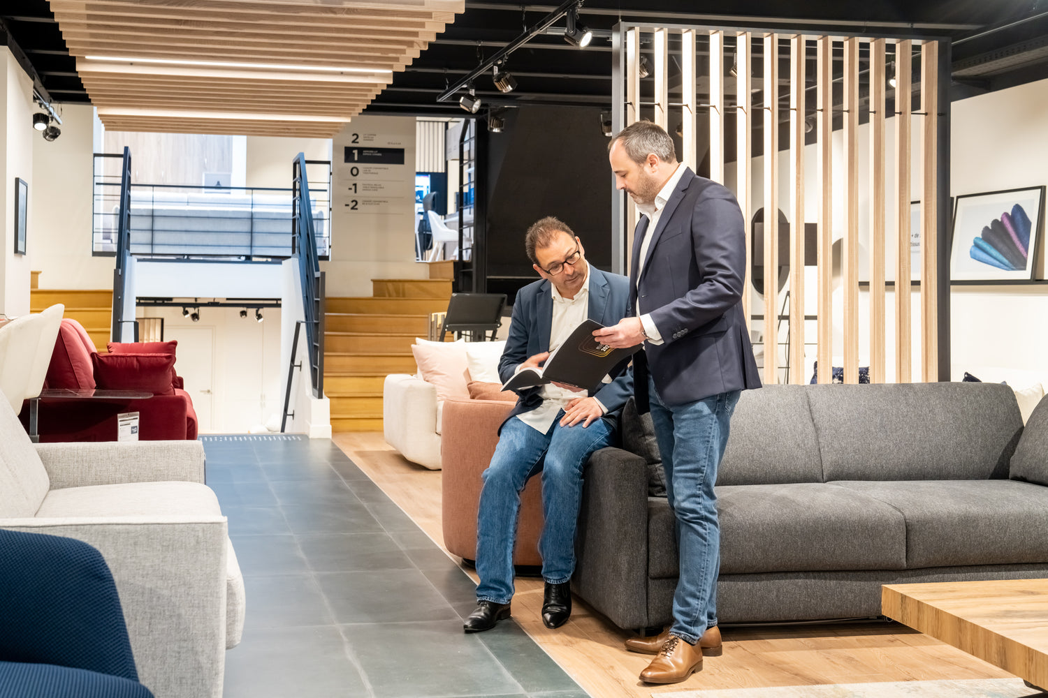 Deux hommes discutent dans un showroom de meubles modernes, entourés de canapés, à La Maison Convertible, 85 avenue Victor Hugo