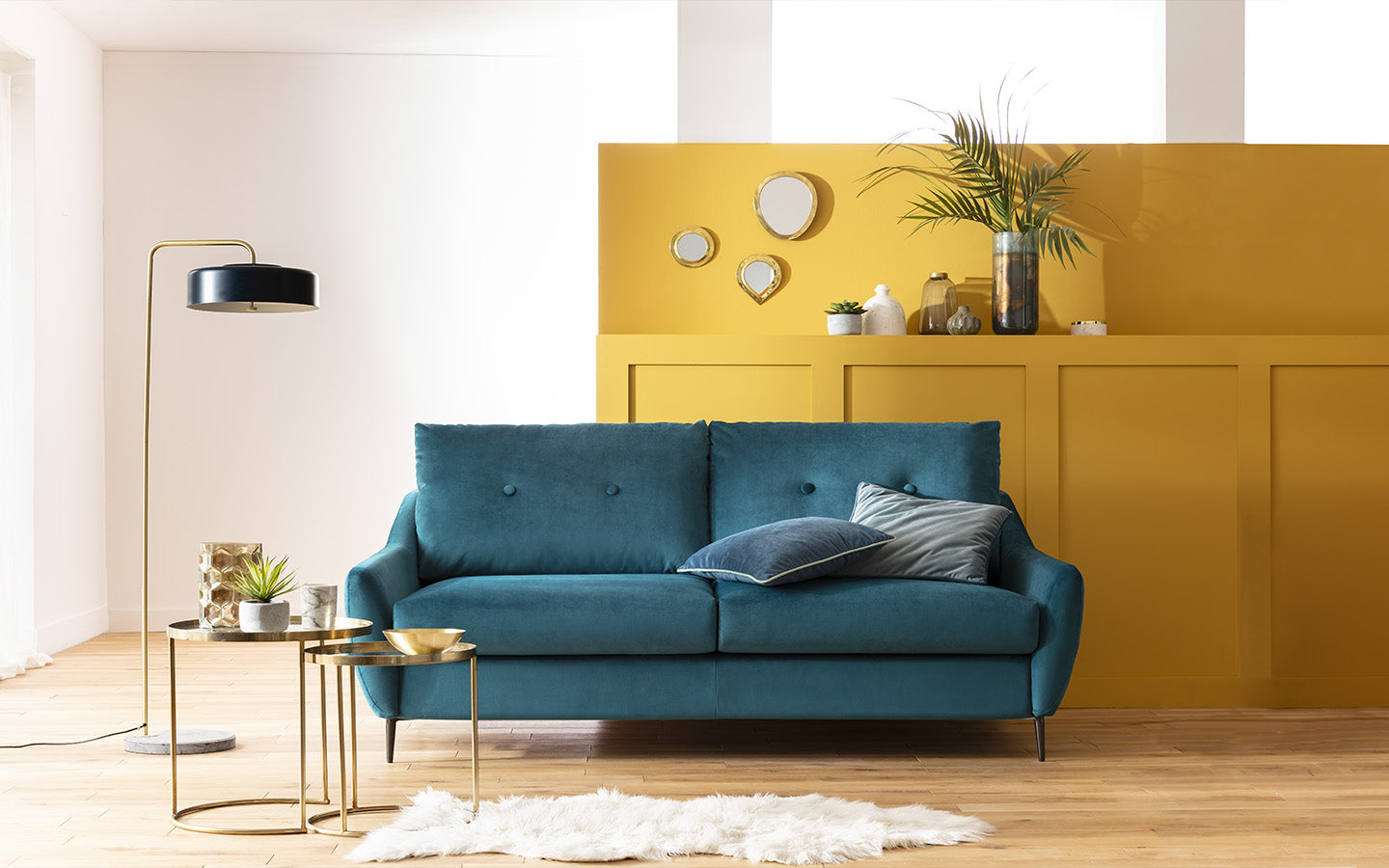 Canapé convertible bleu Layne dans un salon moderne avec mur jaune, lampadaire noir et table basse dorée