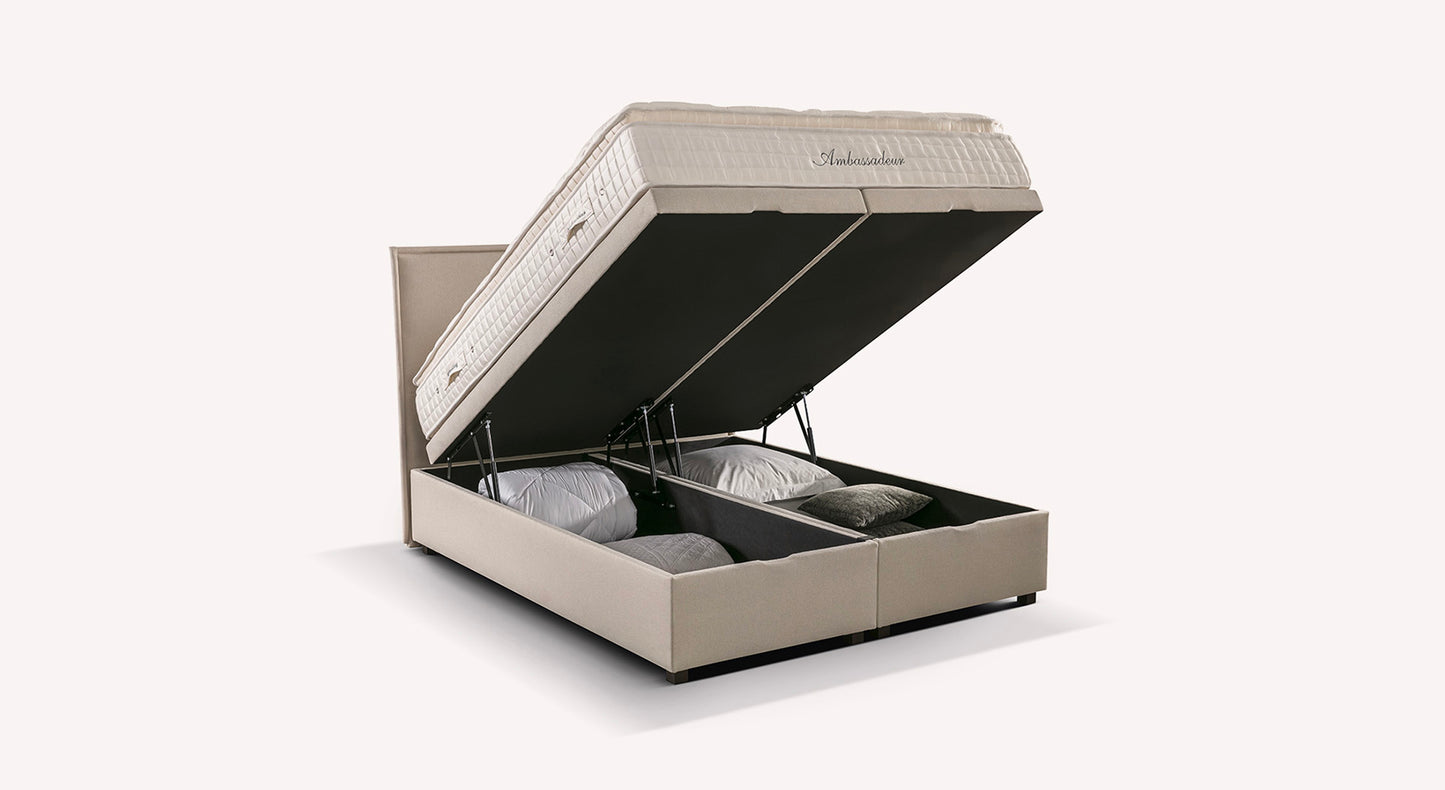 Lit coffre beige modèle Ibiza avec matelas relevé, révélant un espace de rangement contenant des oreillers et des couvertures