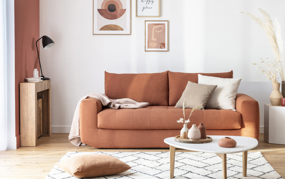 Canapé convertible Stella en tissu terracotta, décoré de coussins neutres, dans un salon moderne avec table basse et œuvres d'art abstraites