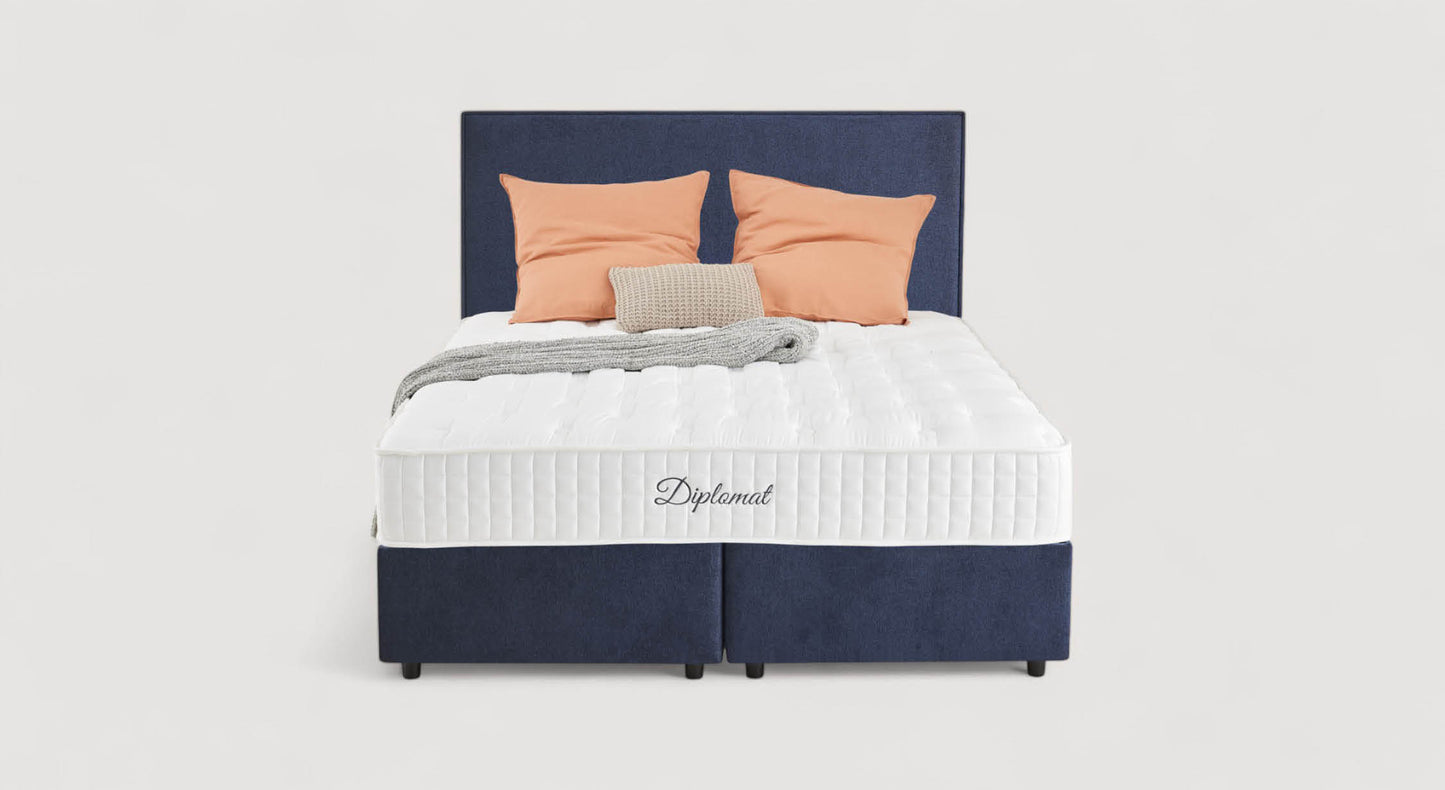 Lit avec tête de lit bleu marine, matelas Diplomat, coussins orange et beige, couverture grise. Modèle Nina Margon Basic 429