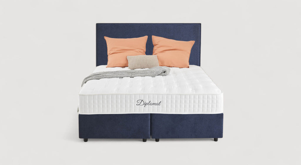 Lit avec tête de lit bleu marine, matelas Diplomat, coussins orange et beige, couverture grise. Modèle Nina Margon Basic 429