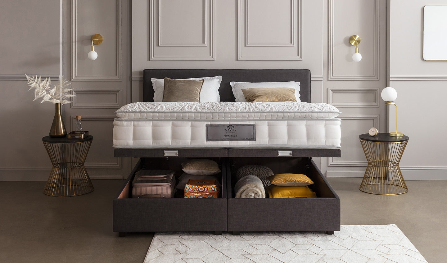 Lit avec matelas Savoy, tiroirs de rangement ouverts contenant des couvertures et oreillers, tables d'appoint dorées, décor élégant