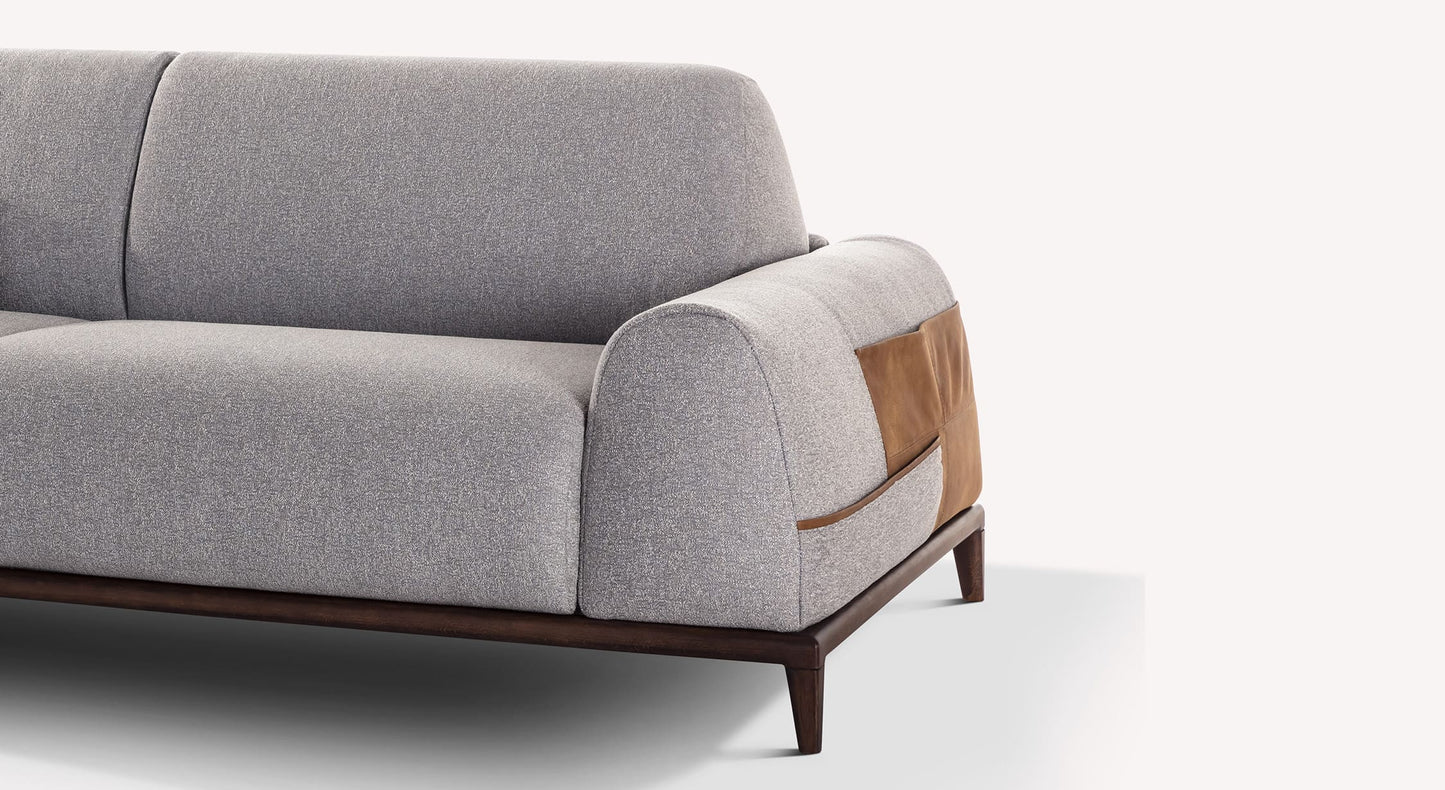 Canapé convertible DARREN Shock Perle en tissu gris clair avec accoudoir arrondi orné d’un détail en cuir marron, pieds en bois foncé, design moderne et épuré.