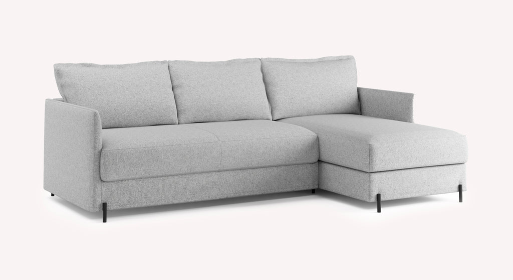 Canapé convertible d'angle gris clair "Serge" de Tixer, avec accoudoirs et pieds noirs, sur fond blanc