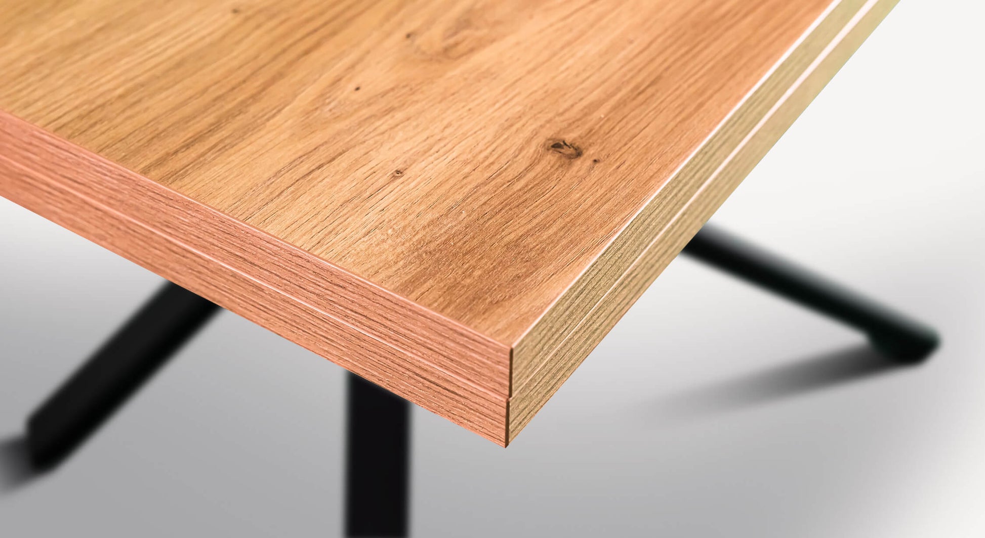 Coin d'une table en bois clair avec des veines visibles, sur un pied noir en métal