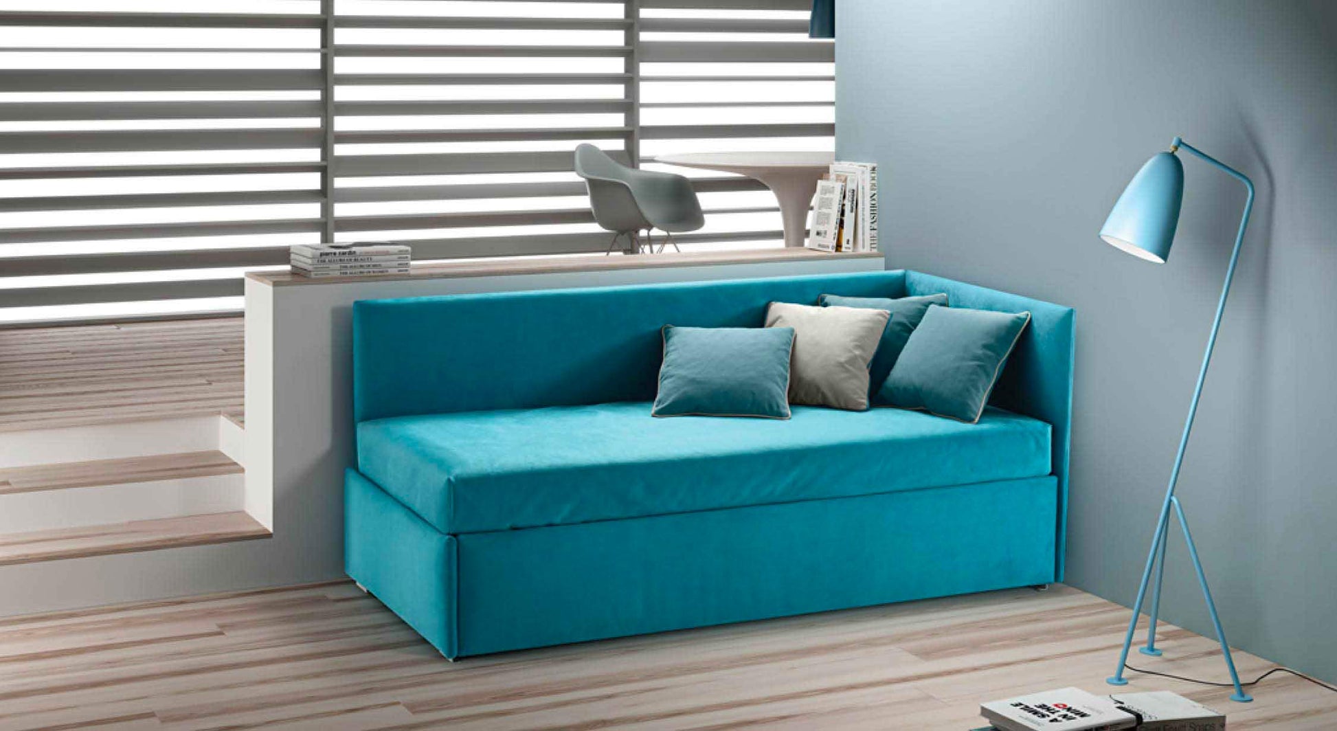 Lit gigogne bleu avec coussins, situé dans un coin moderne et épuré, éclairé par une lampe sur pied assortie