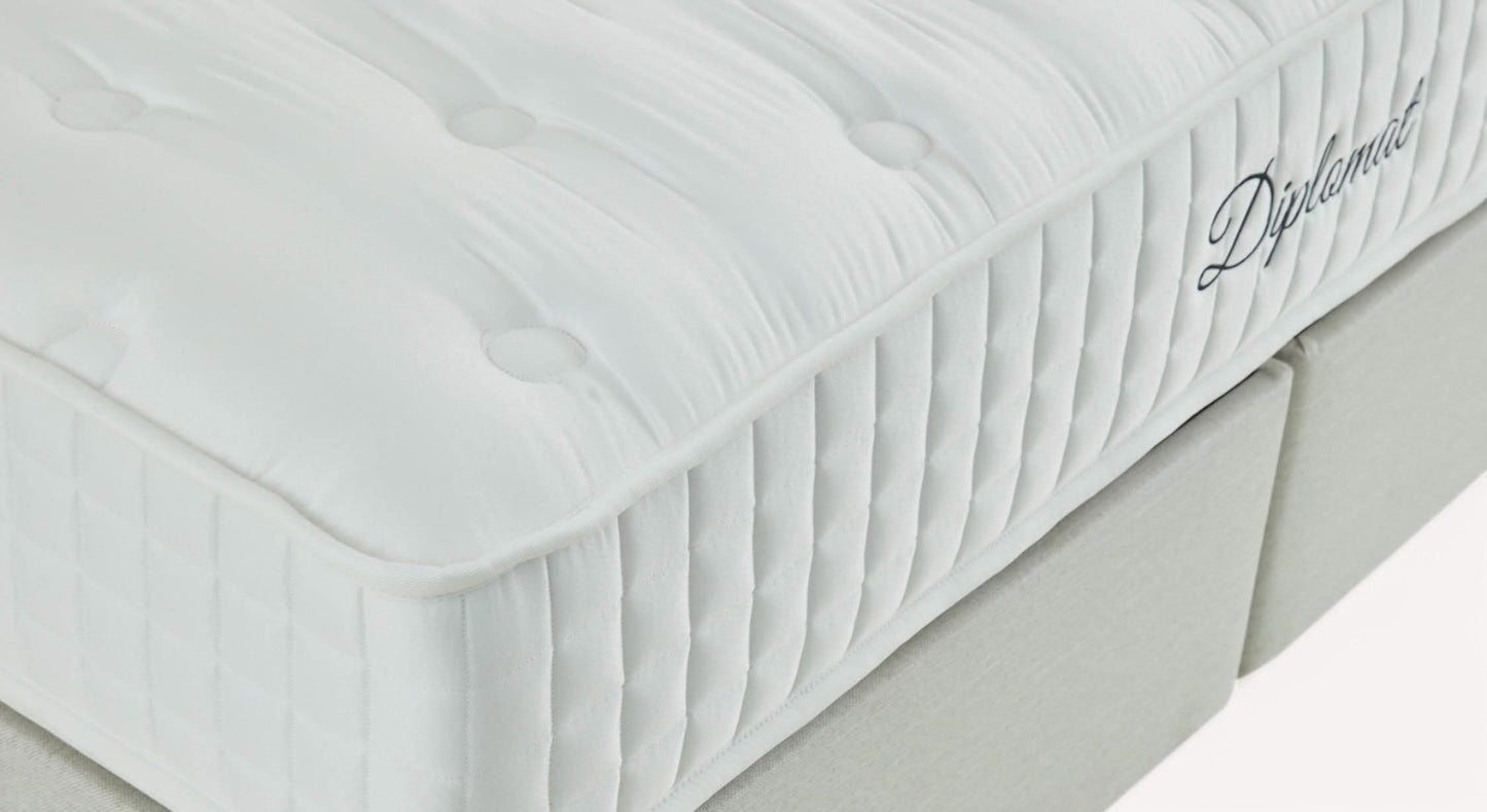 Matelas blanc avec surpiqûres et logo "Diplomat" sur le côté, posé sur un sommier gris clair