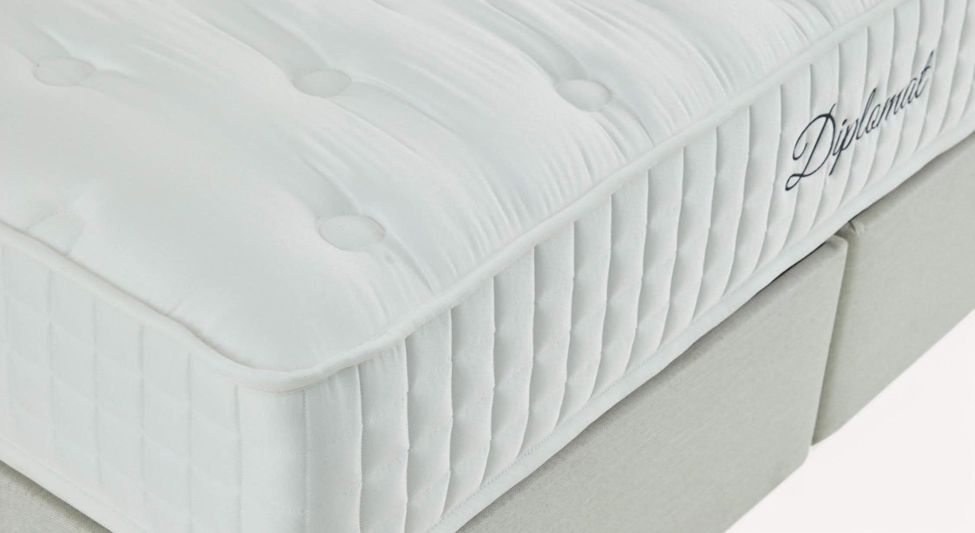 Matelas blanc avec surpiqûres et logo "Diplomat" sur le côté, posé sur un sommier gris clair